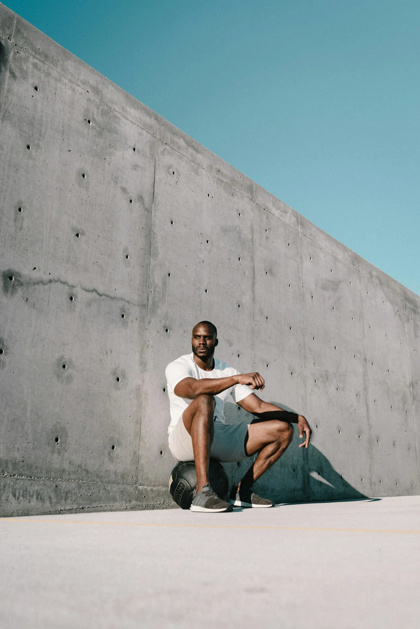 Man crouching against a concrete wall in running gear