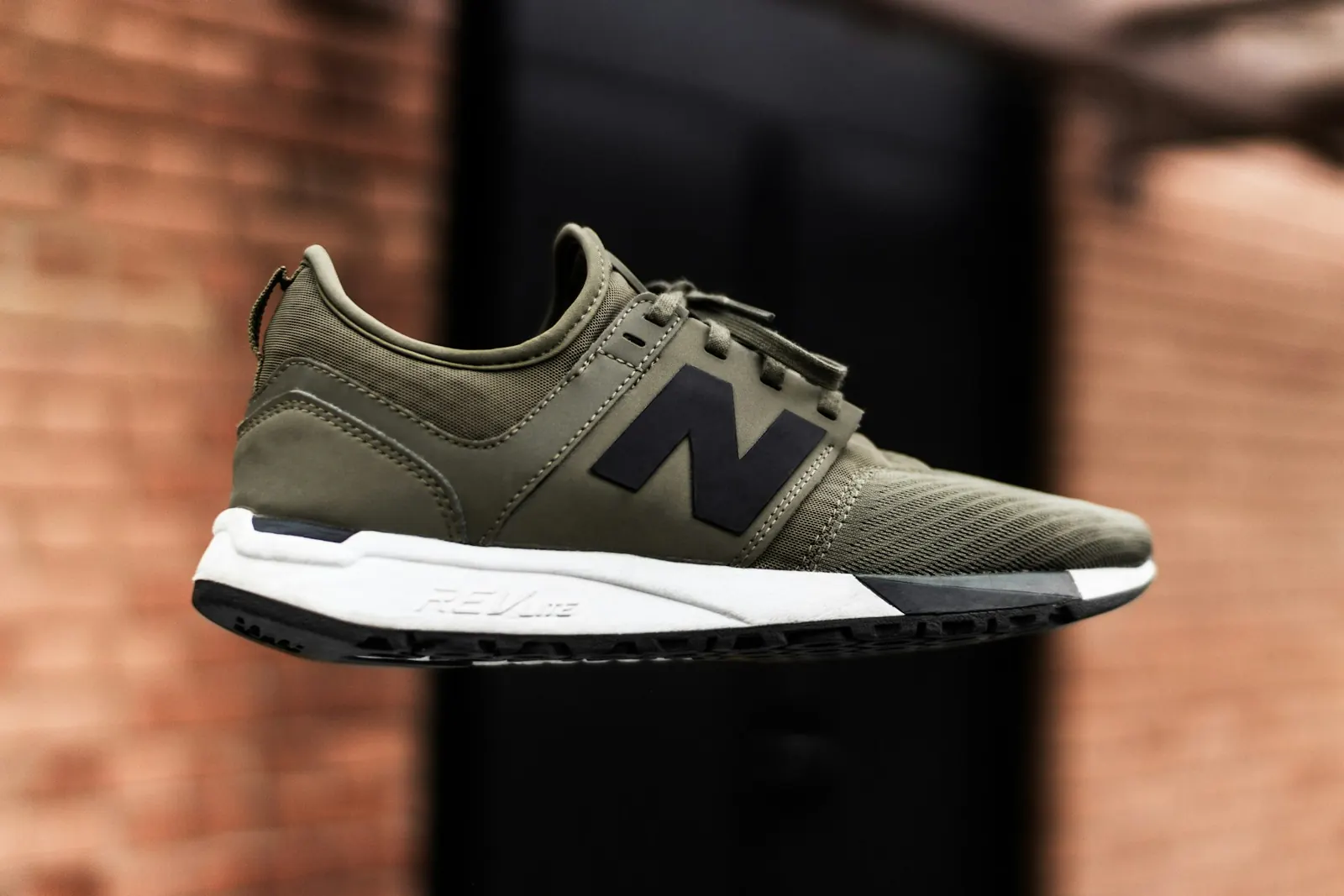 Olive green running shoe floating against a brick wall