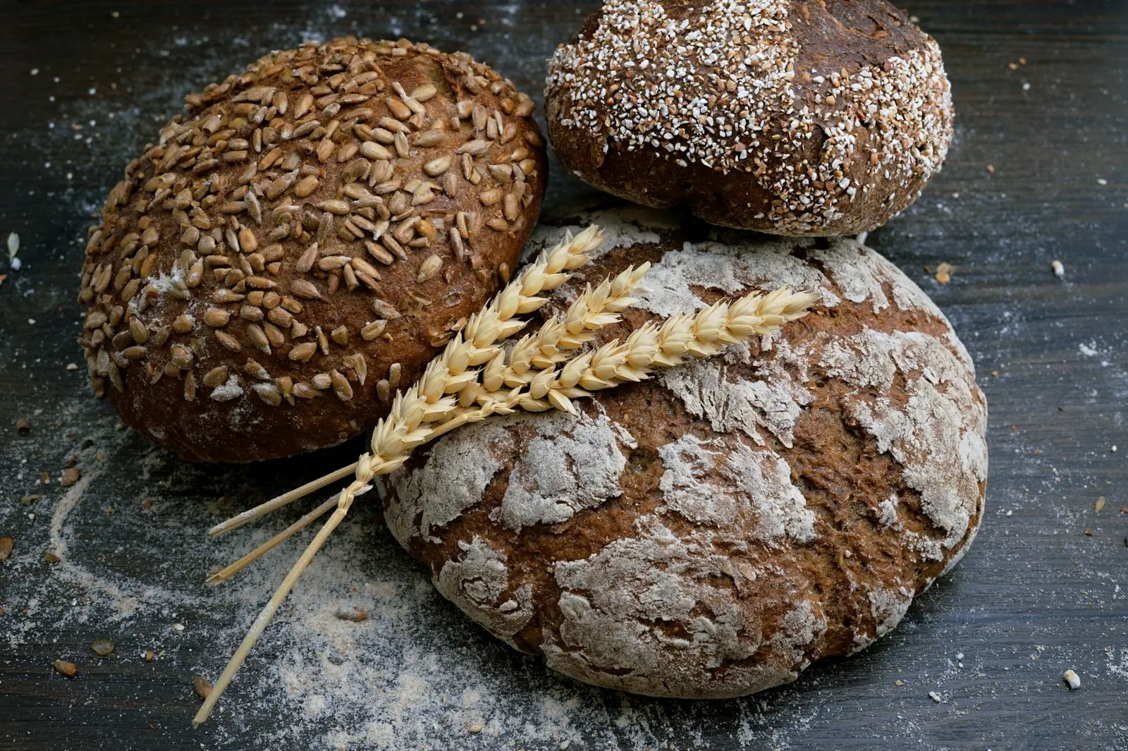 Loaves of rustic bread with wheat stalks on a dark table