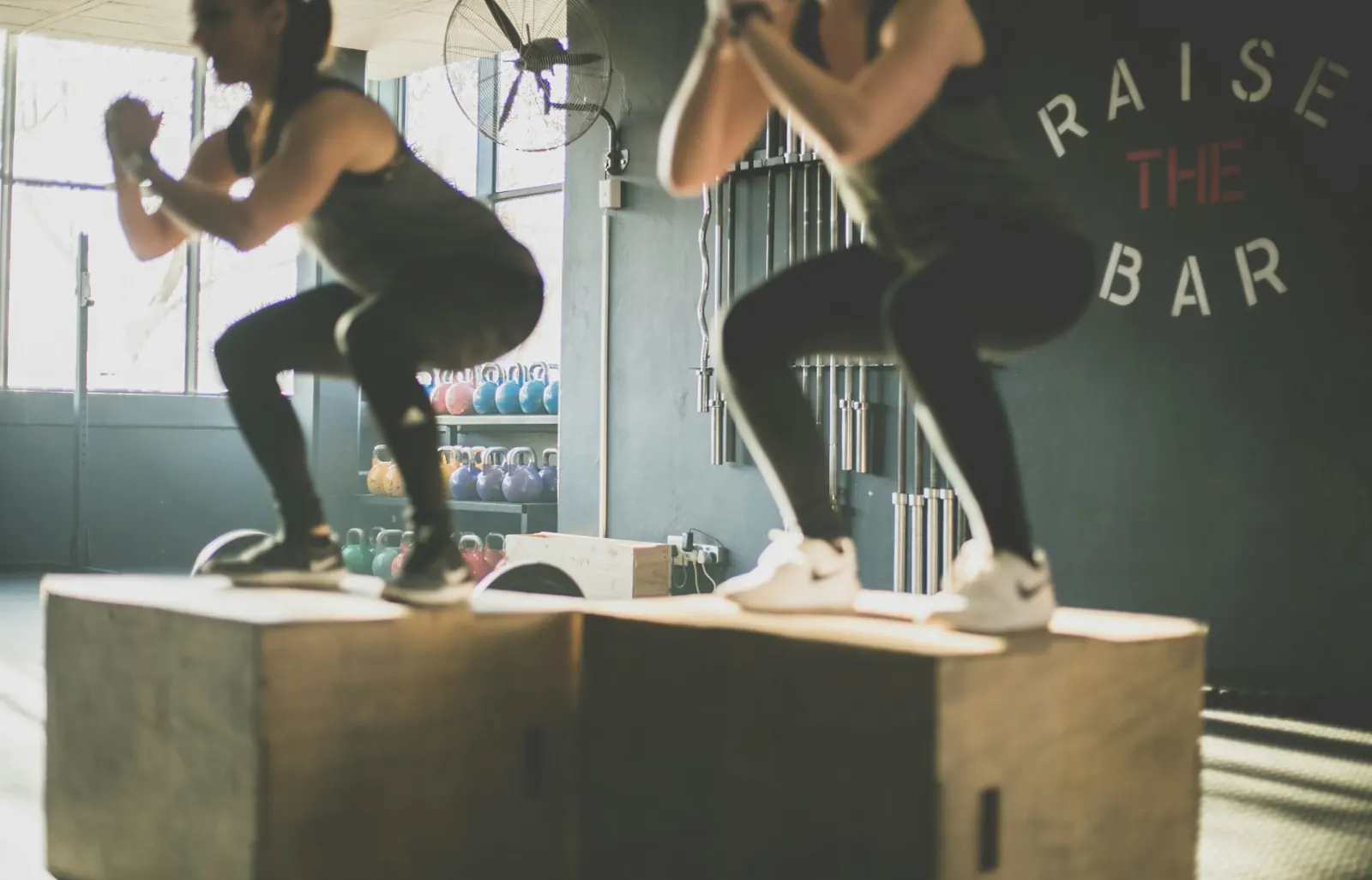 Two people doing box jumps in a gym