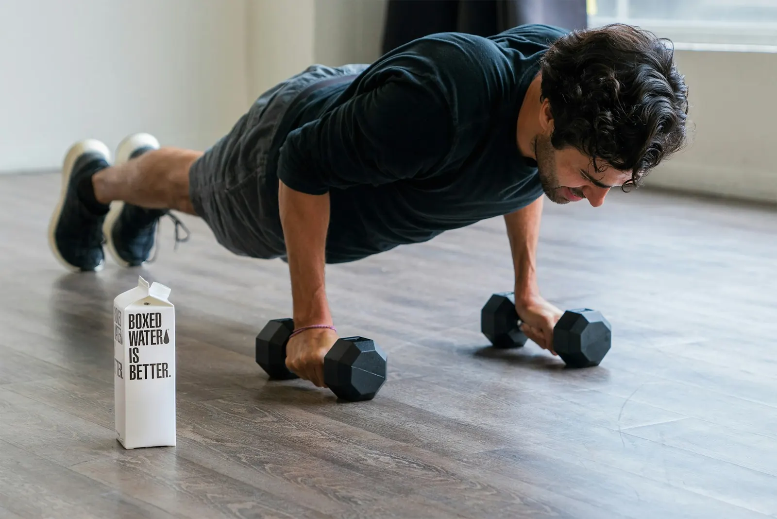 Man doing push-ups on dumbbells beside a carton of water