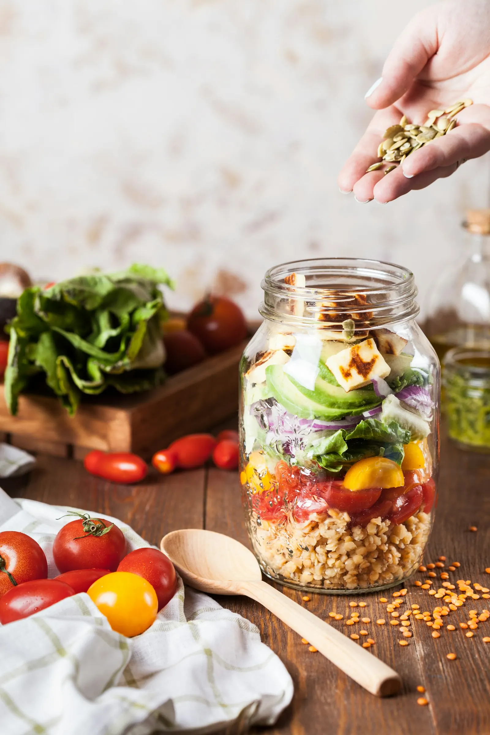 Glass jar of layered salad with chickpeas, tomatoes and greens