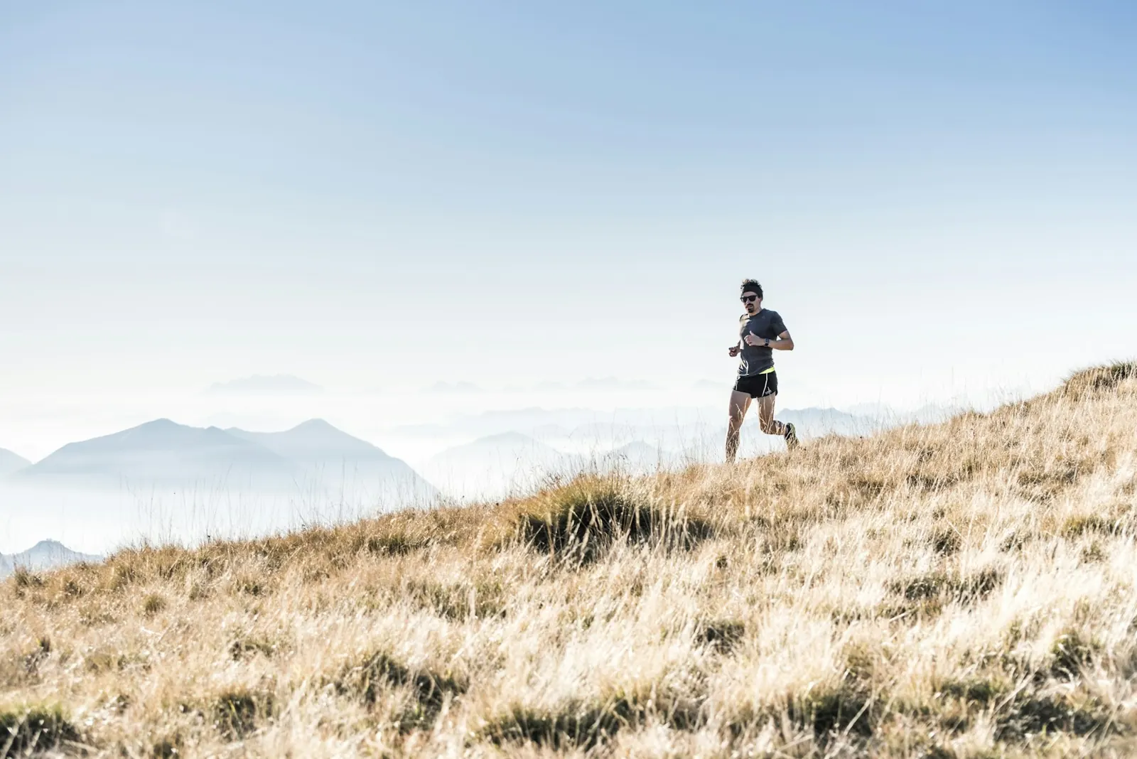 Trail runner climbing a grassy hillside with mountains behind
