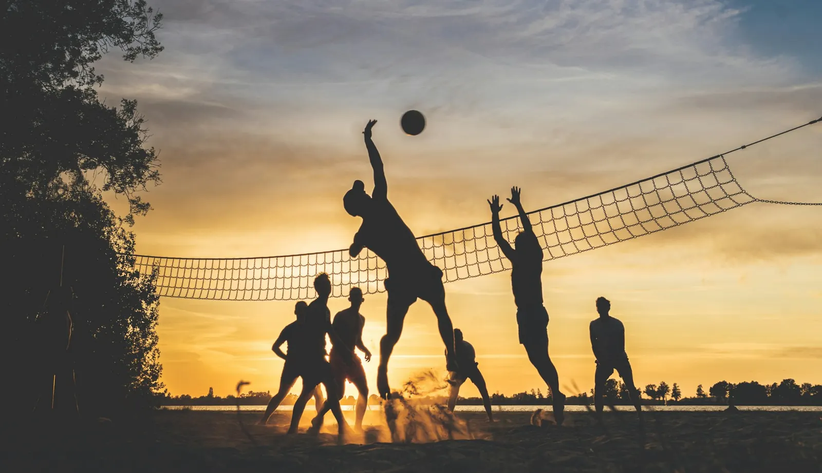 Silhouettes of players jumping at a beach volleyball net at sunset