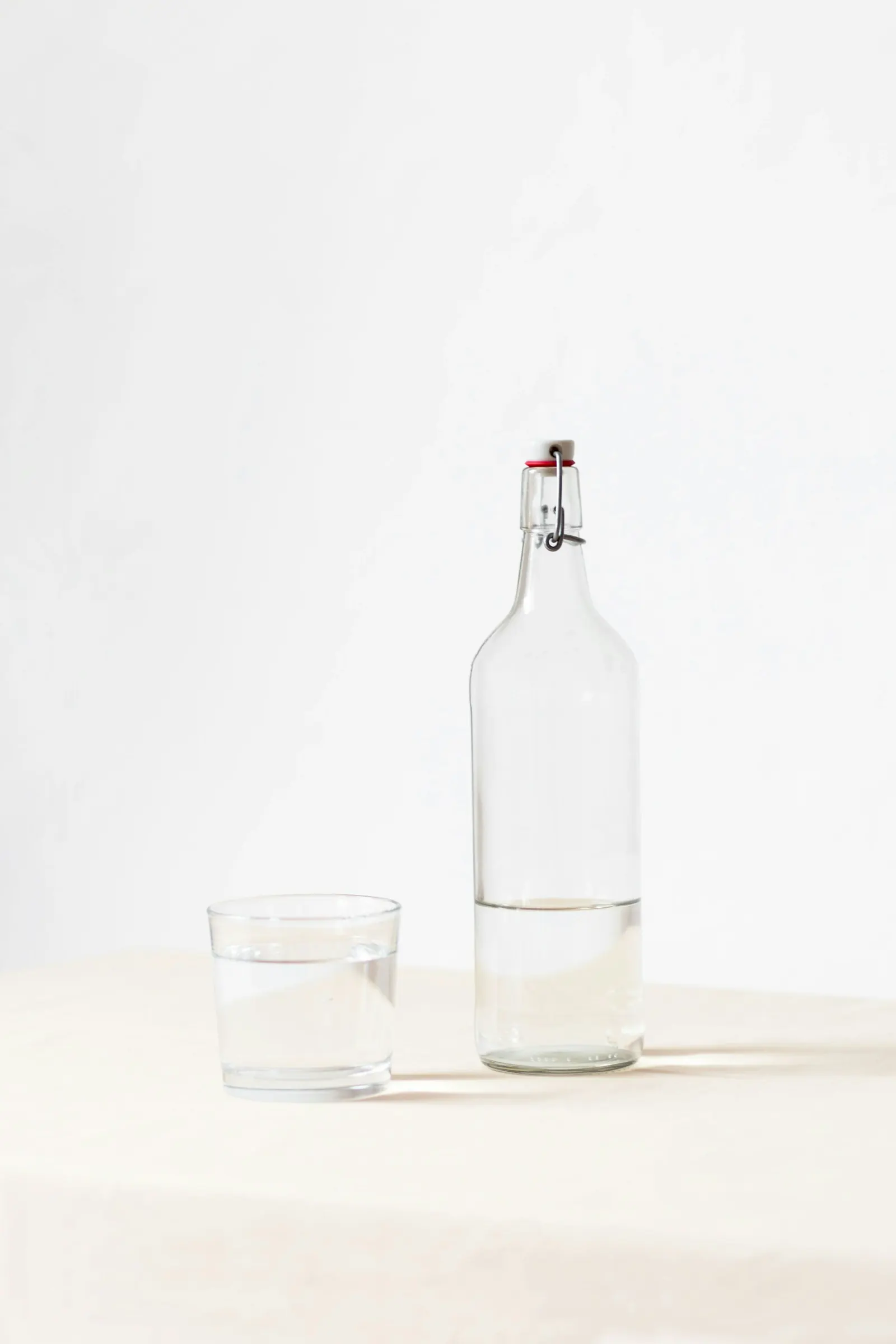 Glass bottle of water next to an empty glass on a white surface