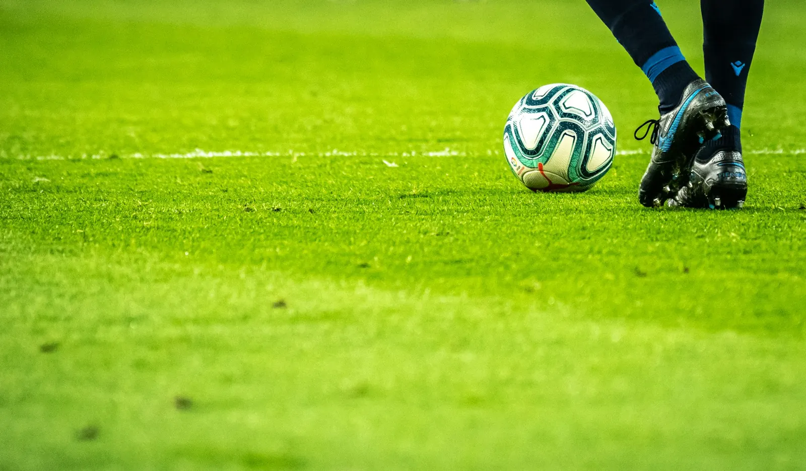 Football player's boot next to a ball on a green pitch