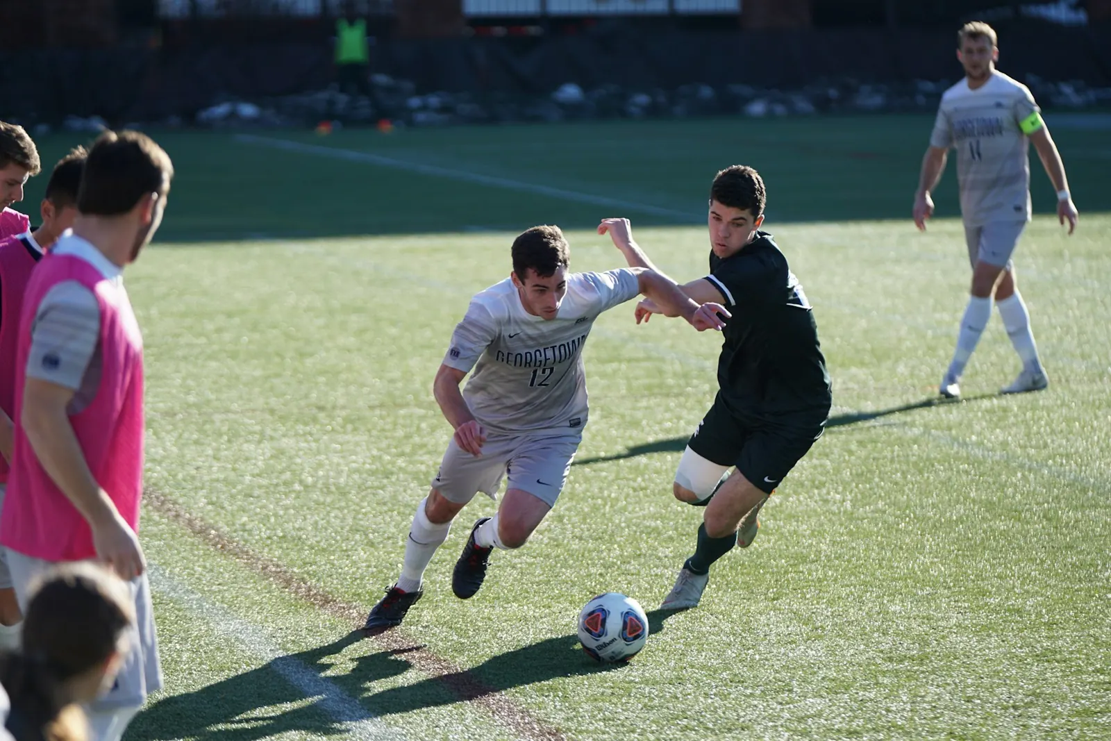 Footballers competing for the ball during a match on a sunny pitch