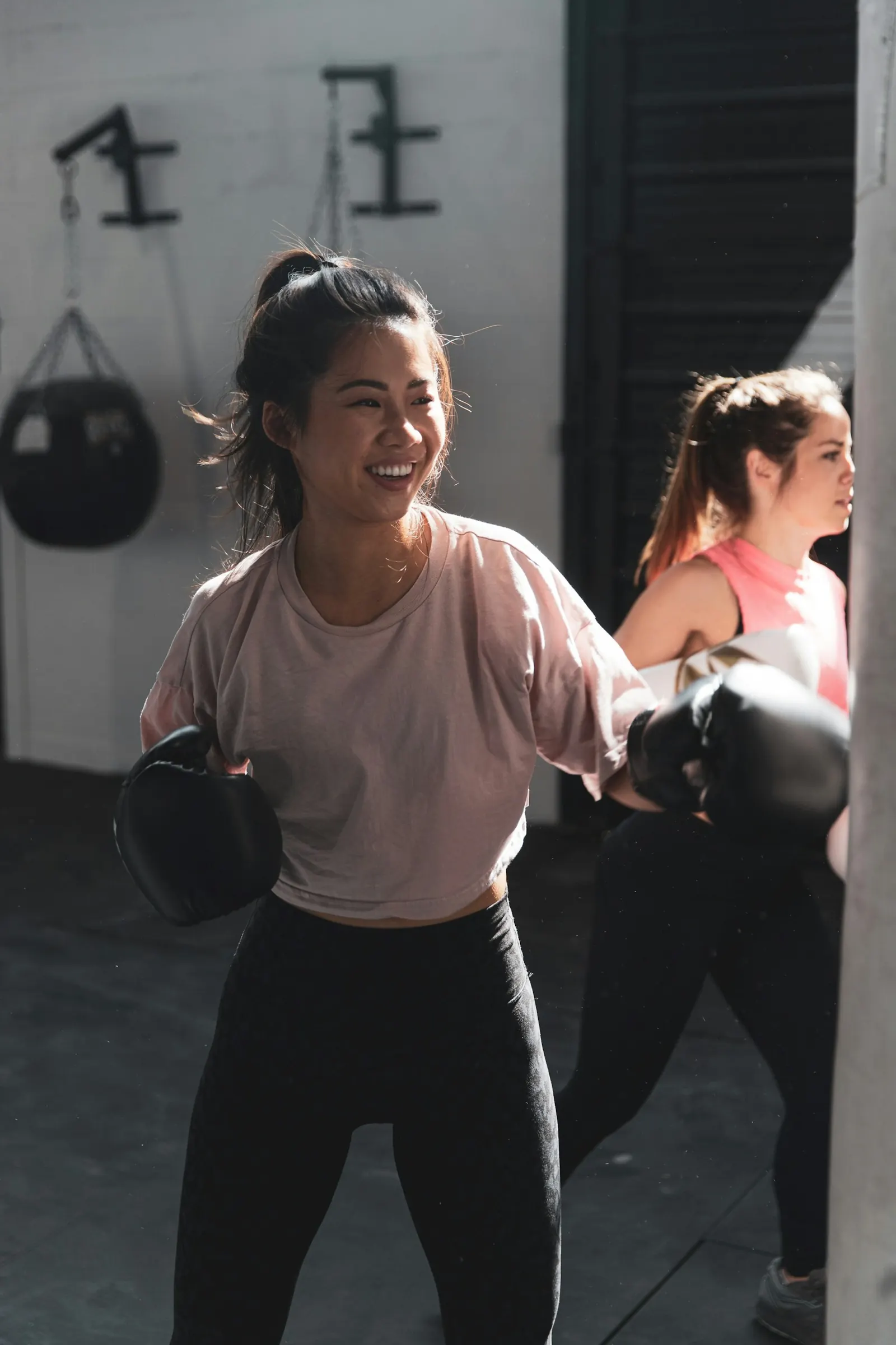 Two women laughing during a boxing workout in a gym