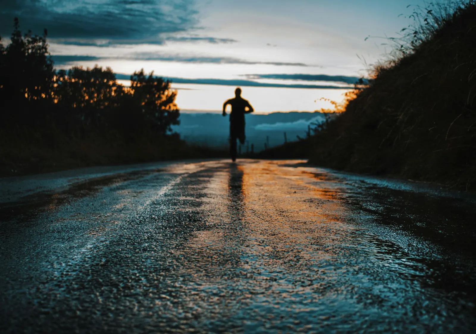 Runner silhouetted on a wet road at sunset with hills behind