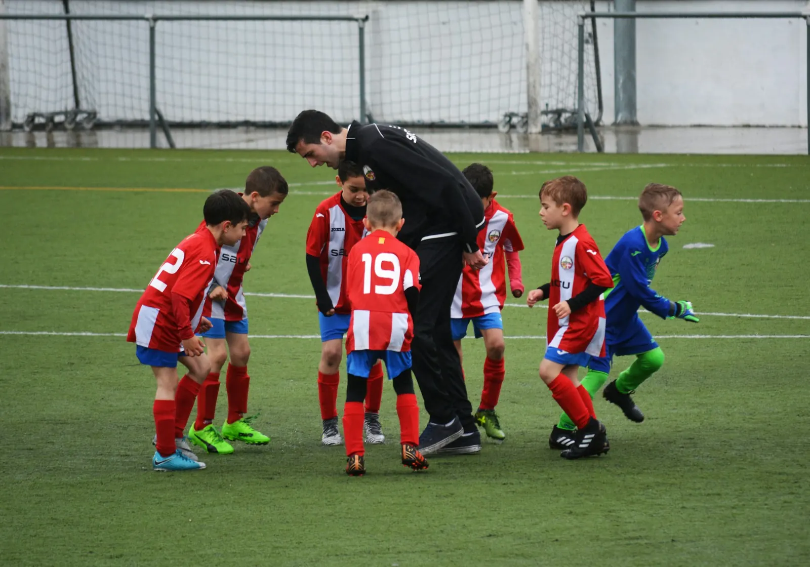 Youth football coach talking to his players in a huddle on the pitch