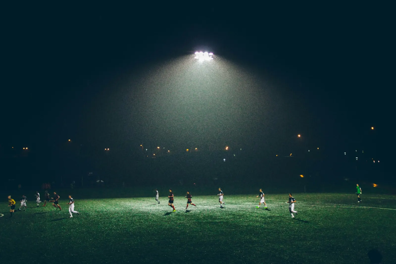 Football match being played under floodlights at night seen from a distance