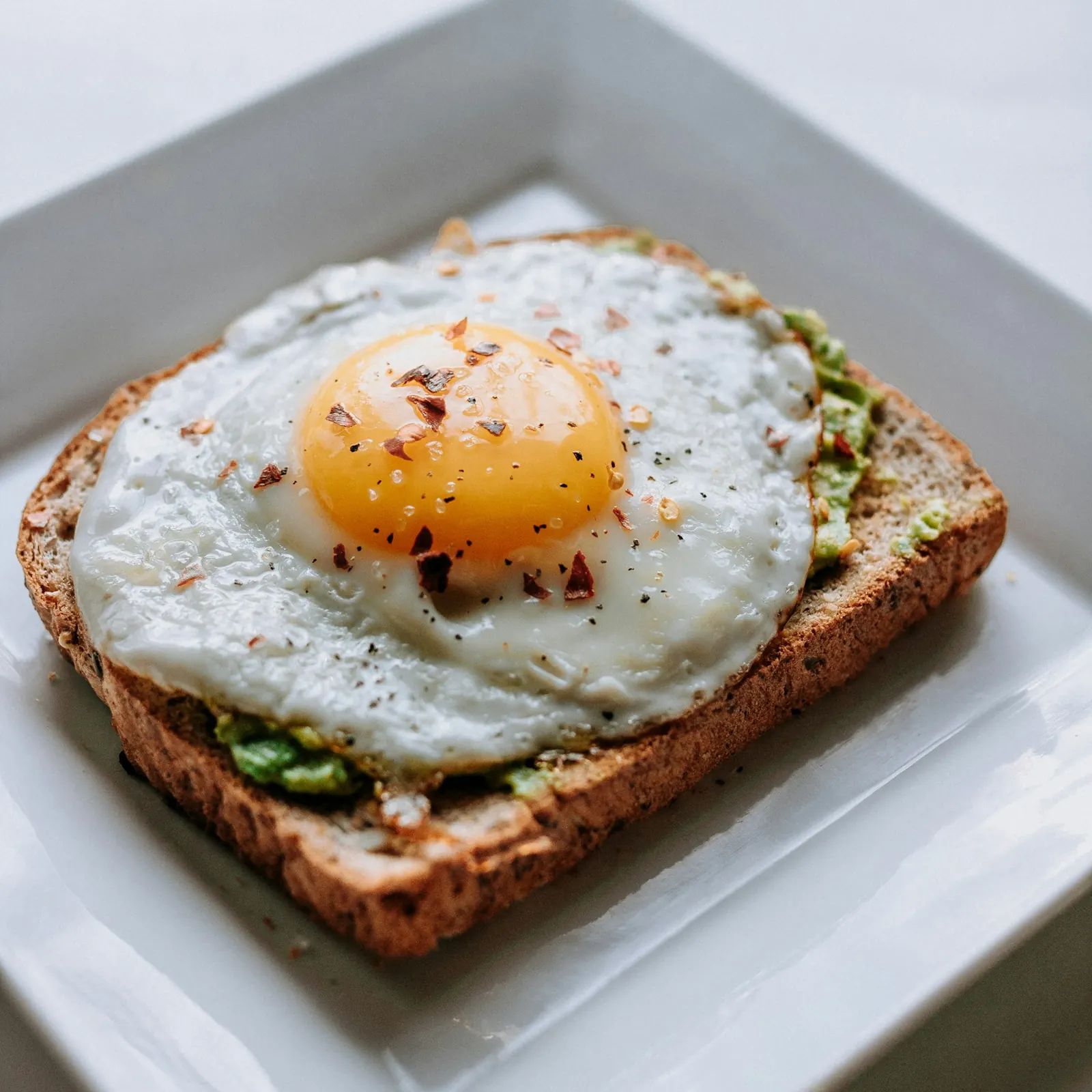 Fried egg on toast with avocado on a square plate