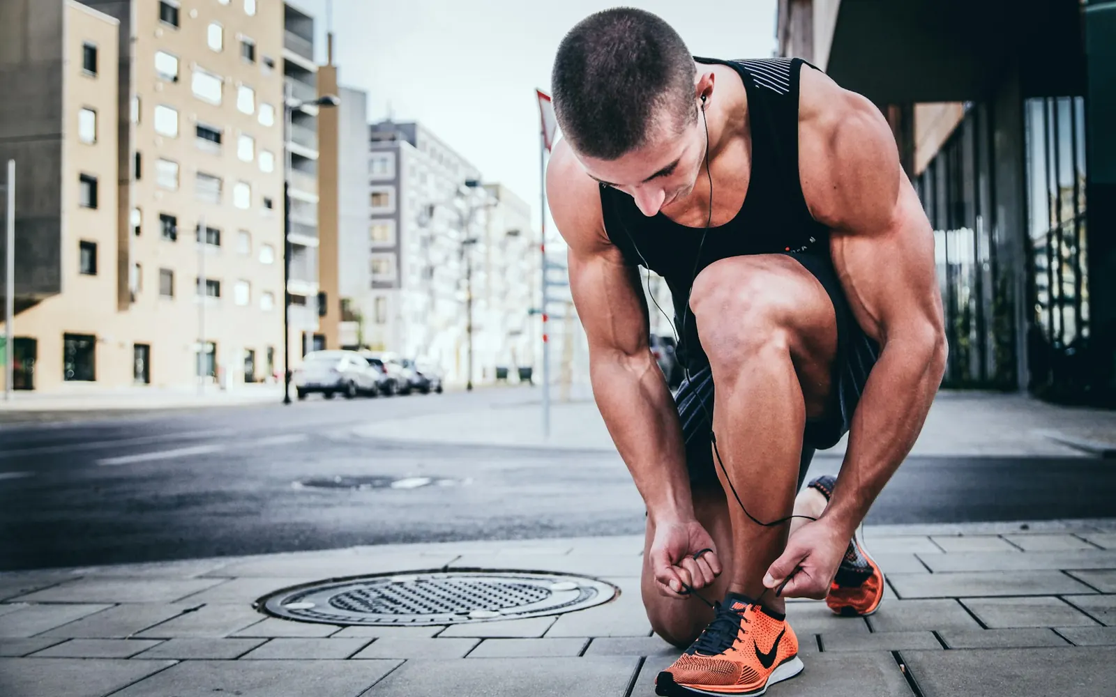 Athlete crouching to tie his running shoes on a city street