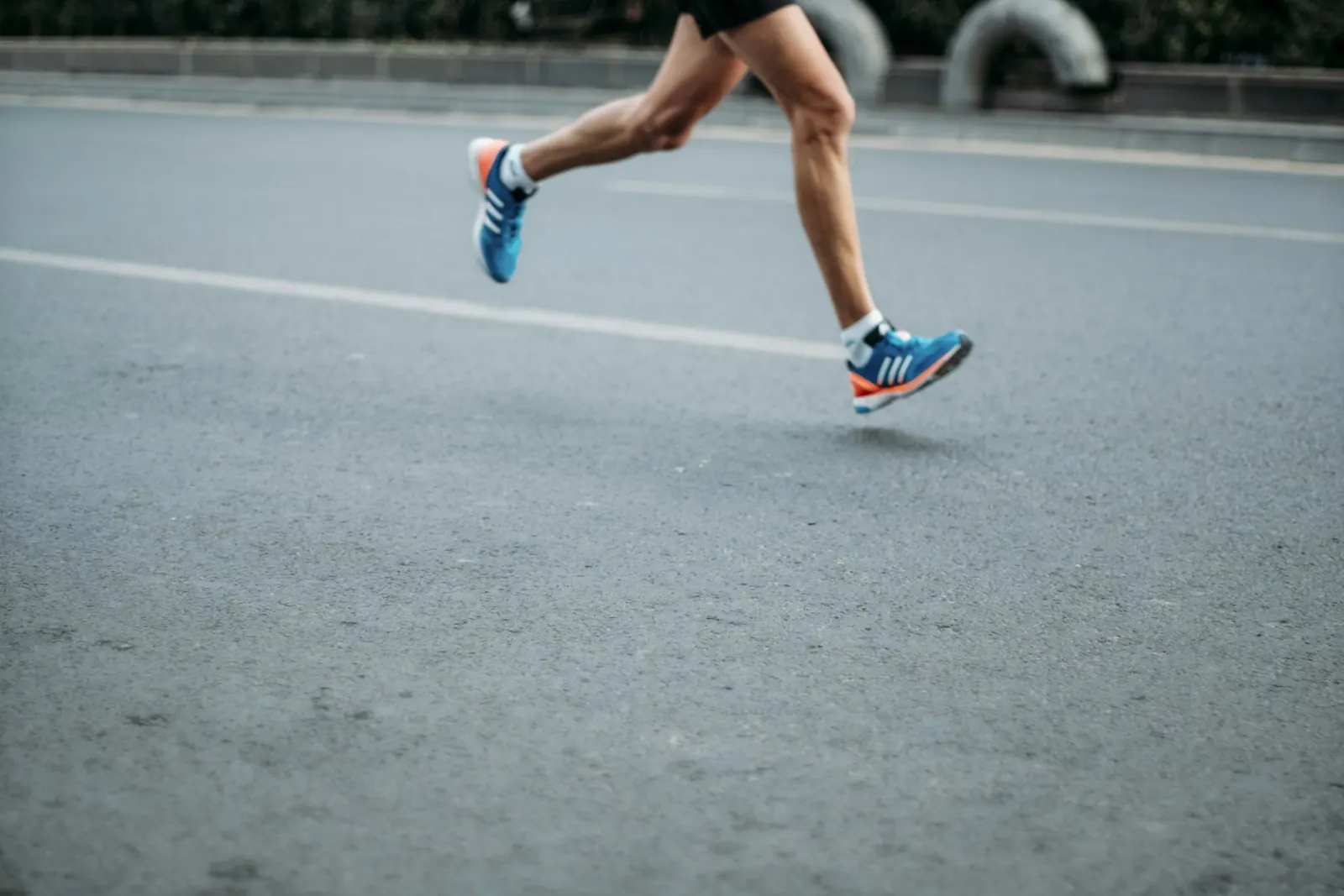 Close-up of a runner's legs and shoes mid-stride on an asphalt road