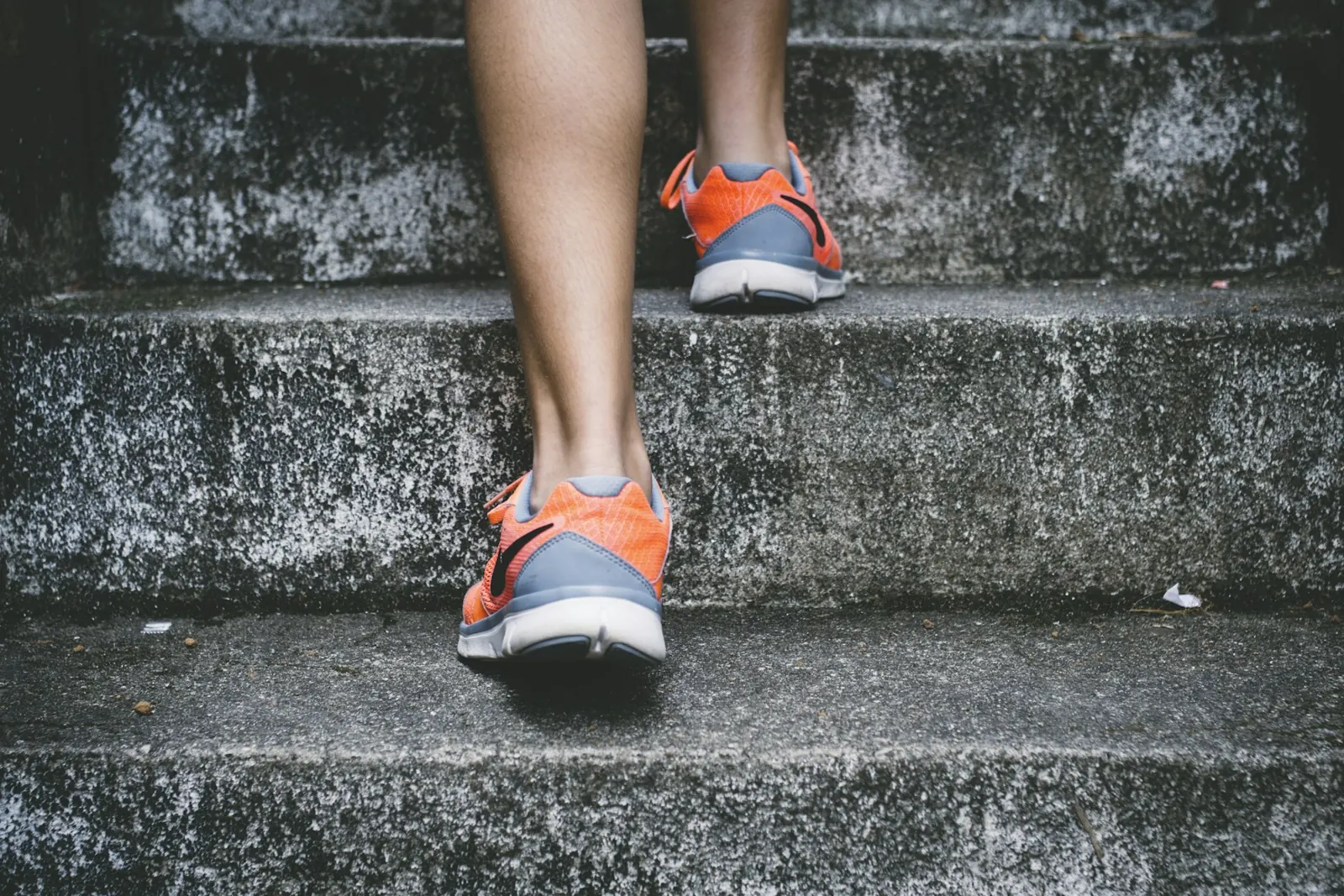 Runner's legs and orange running shoes climbing concrete steps