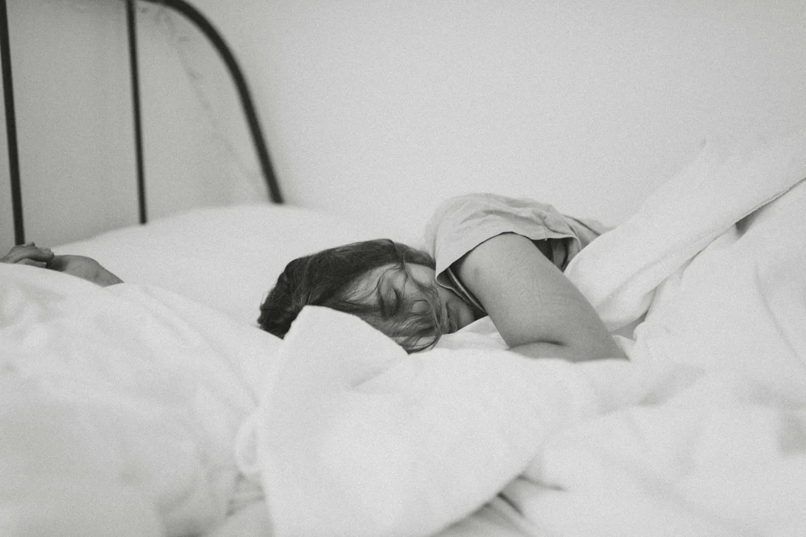 Person sleeping under white sheets, black and white photo