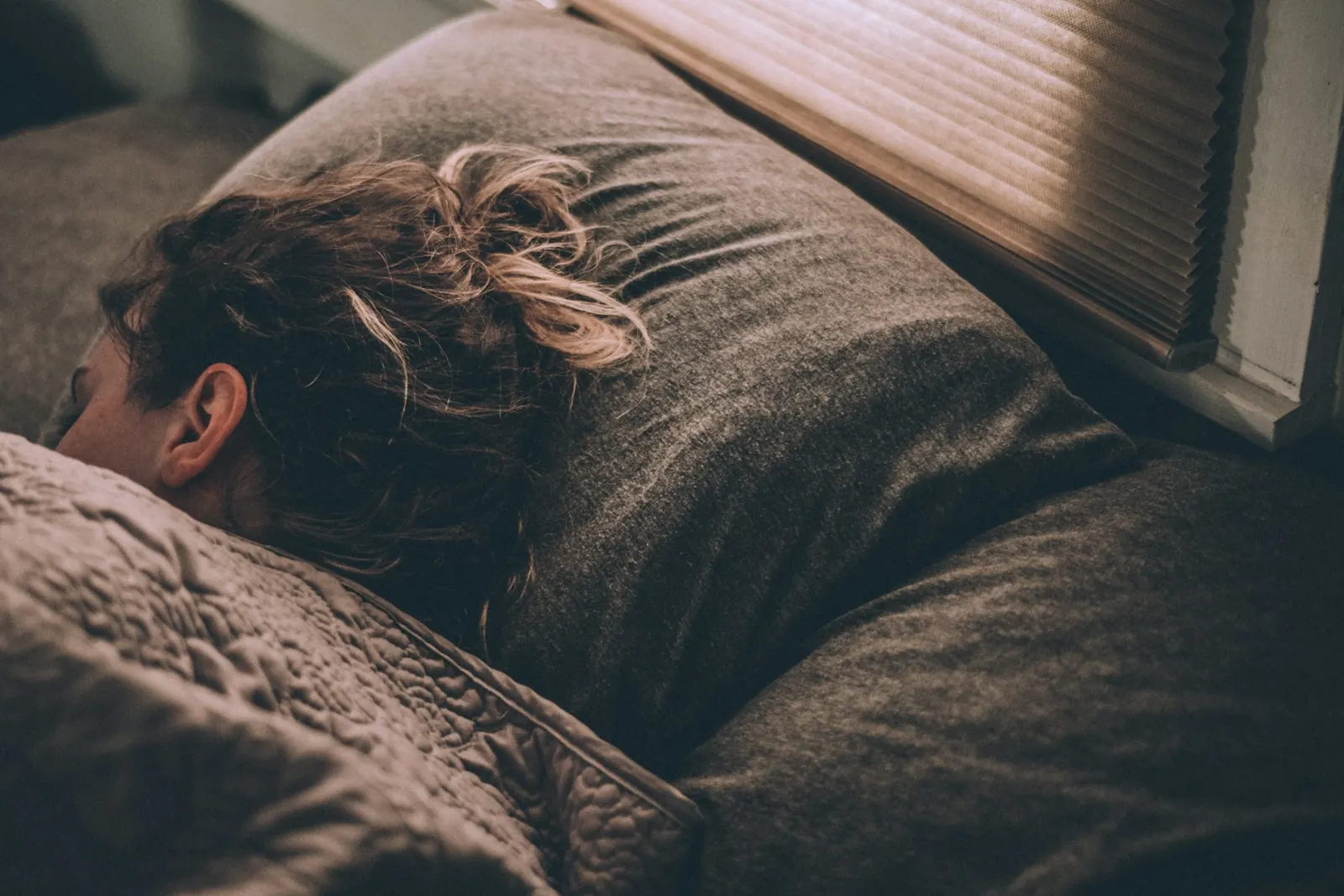 Person asleep in a dark bedroom with their head on a pillow