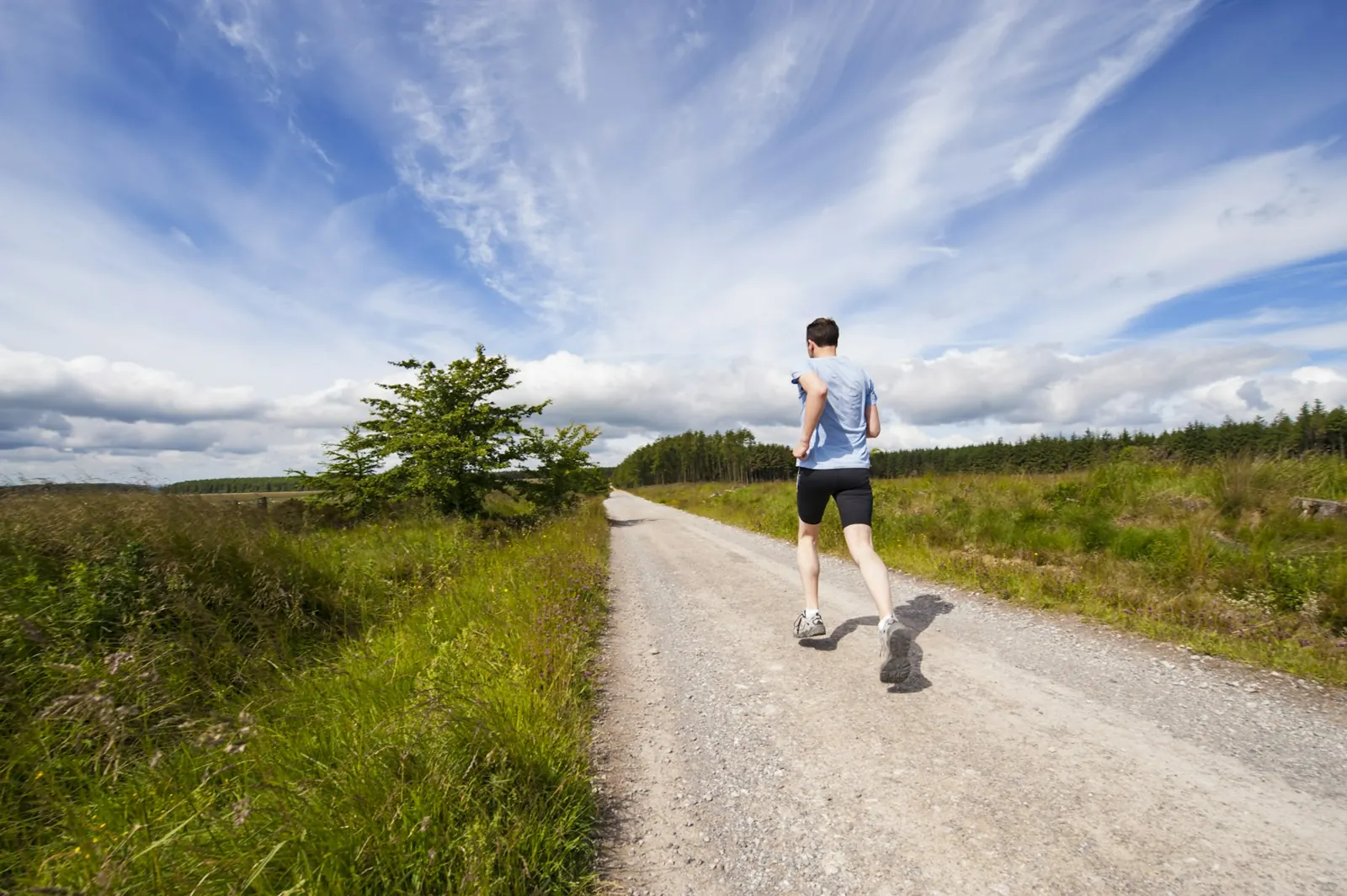 Runner jogging alone along a quiet gravel road through green fields