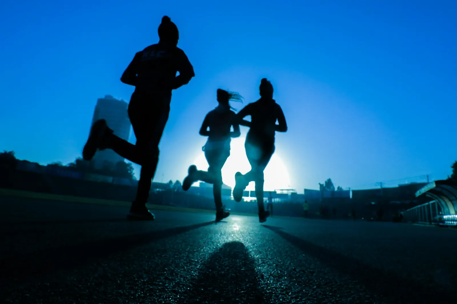 Three runners silhouetted against a blue evening sky on a running track